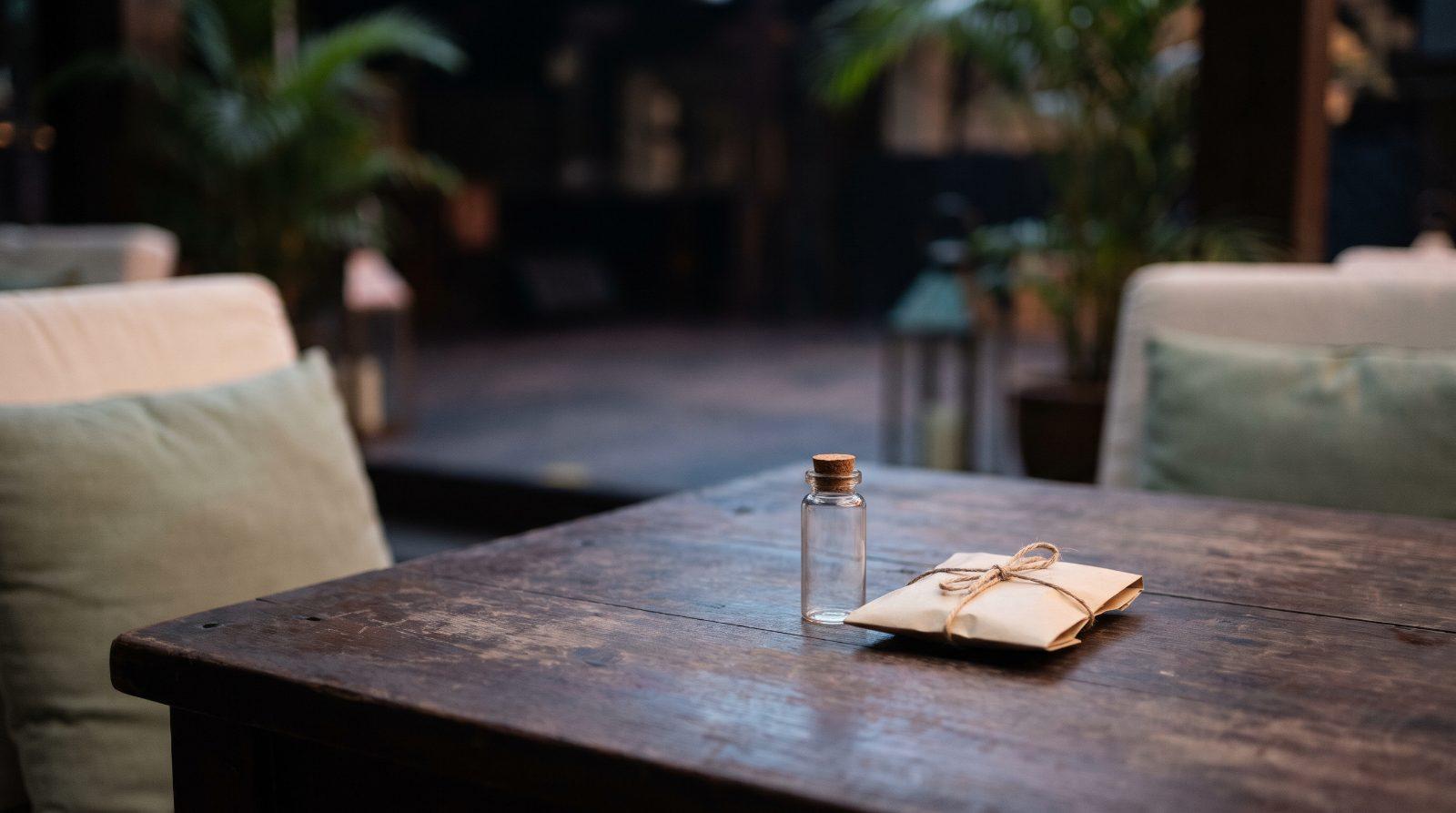A small empty glass vial and a folded paper sachet on a dark wooden table in a dim lounge